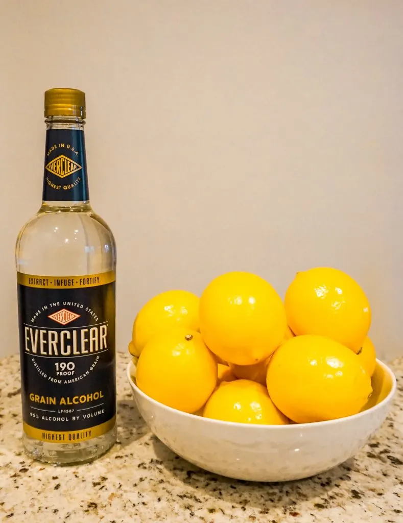 A bottle of Everclear and a bowl of Meyer lemons next to it.