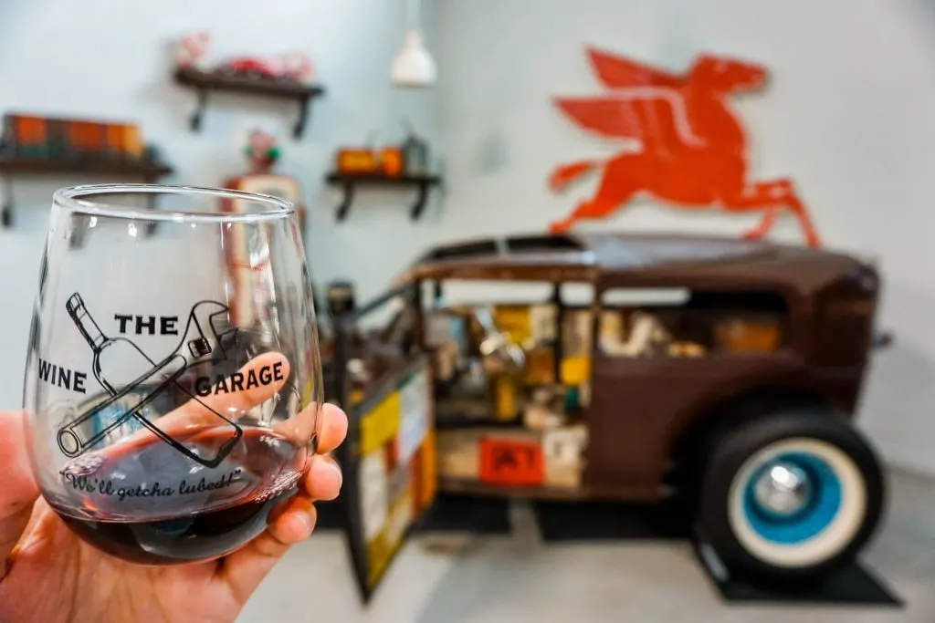 A stemless glass of red wine with a Rat Rod classic car in the background at The Wine Garage in Fredericksburg, Texas.