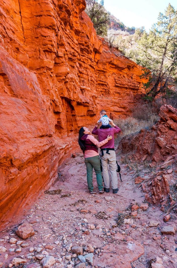 A hiking couple with their baby exploring a red rock fin formation at Caprock Canyons State Park.