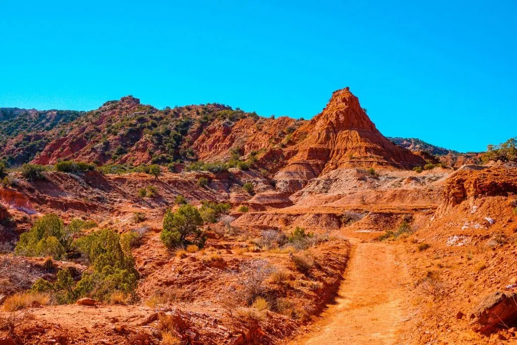 A red dirt hiking trail with red rock formations at Caprock Canyons State Park.
