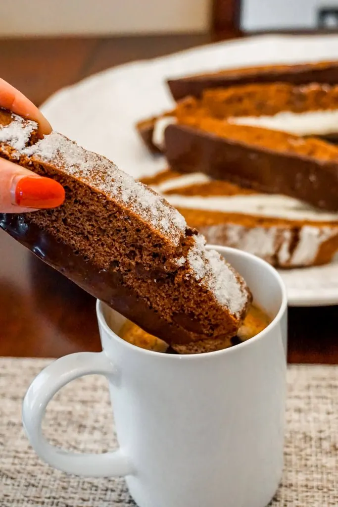 A hand dunking a Triple Chocolate Biscotti in a cup of hot coffee.