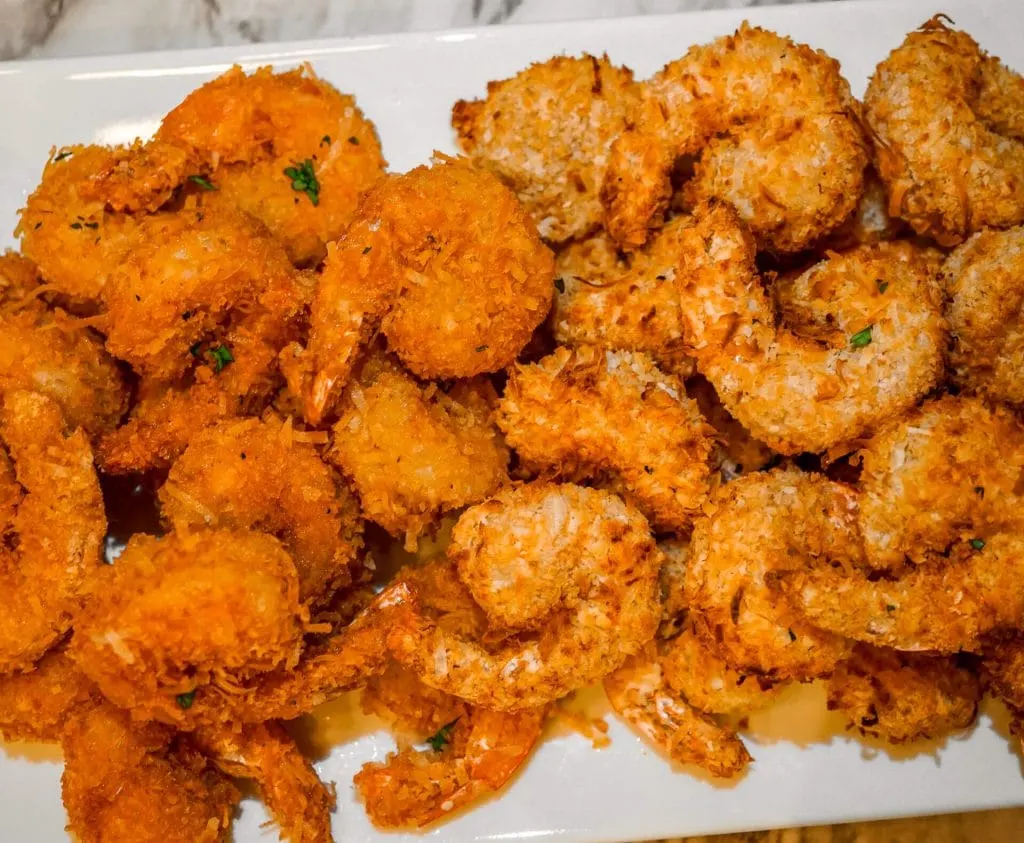 A plate of two different fried coconut shrimp. On the left is coconut shrimp fried in oil. On the right is coconut shrimp fried in an air fryer.