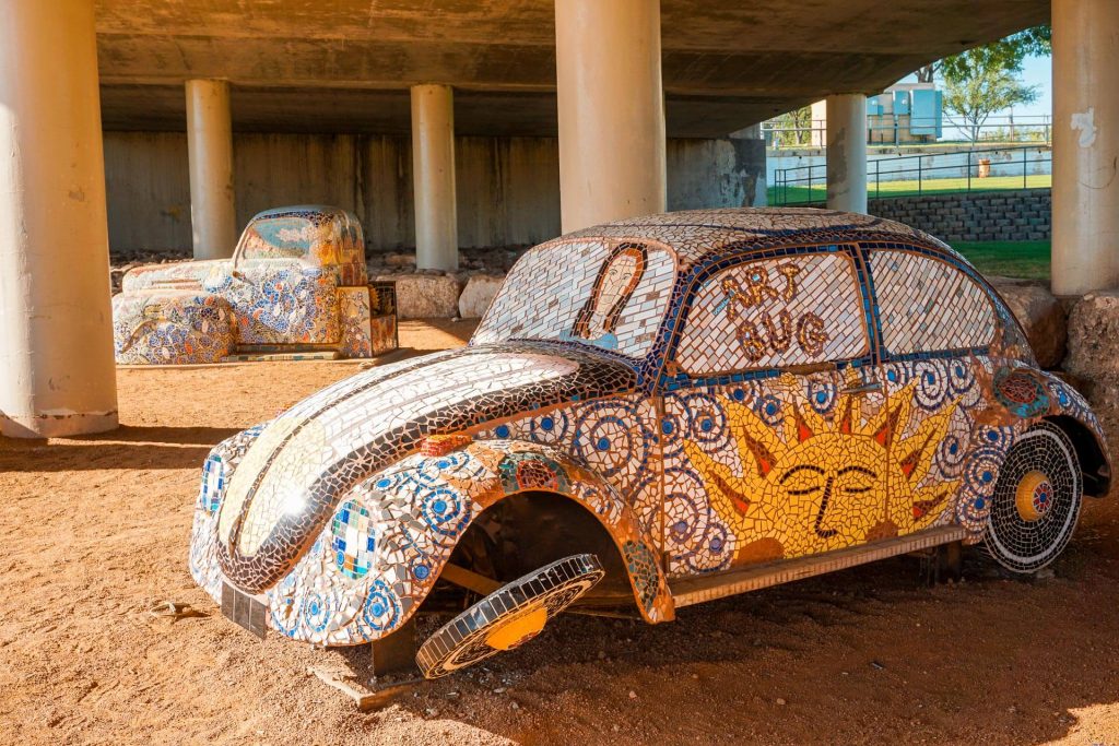 A mosaic Volkswagon beetle and a mosaic pick up truck under a bridge in San Angelo. Finding these mosaic sculptures is one of the best things to do in San Angelo.