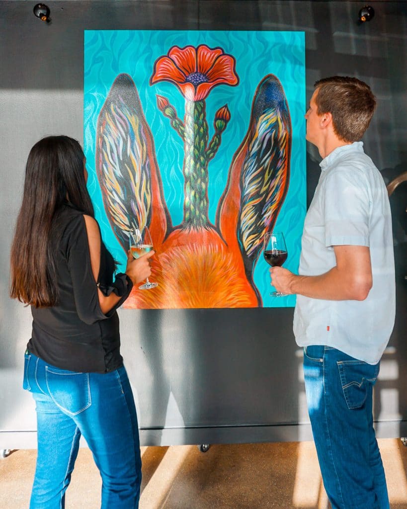 One of the best things to do in San Angelo is enjoy fine art and wine. Pictured is a couple with wine in their hands while admiring a piece of artwork at Raw 1899.