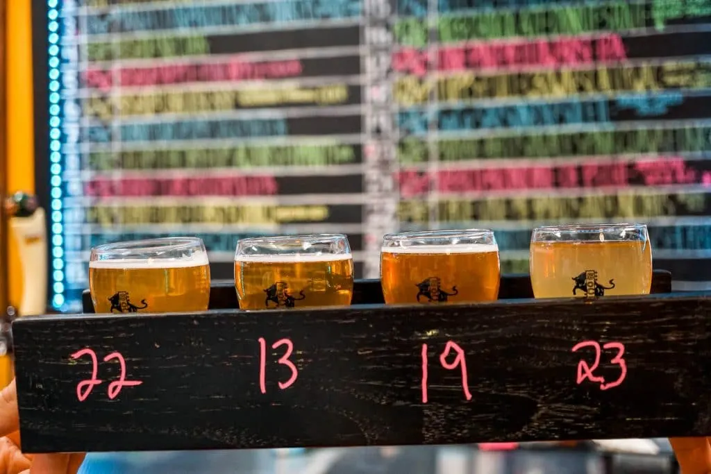 A beer flight of four glasses with a neon beer wall in the background from SoCo Brewery in San Angelo.