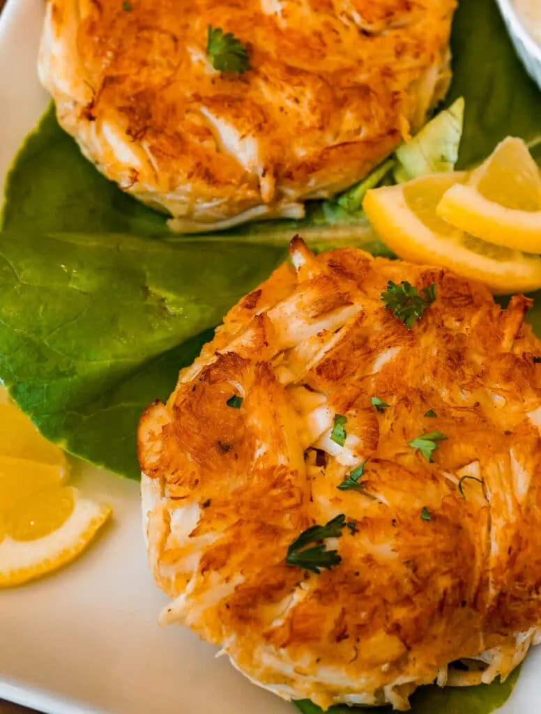 A Maryland Crab Cake with parsley on top and lemon triangles on the side.