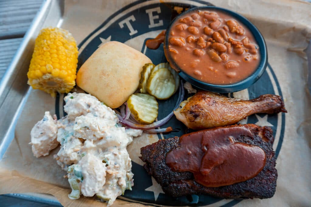 A platter of potato salad, corn on the cob, biscuit, ribs, chicken leg, and a bowl of beans from the Chuckwagon Dinner at The Silver Spur Resort.