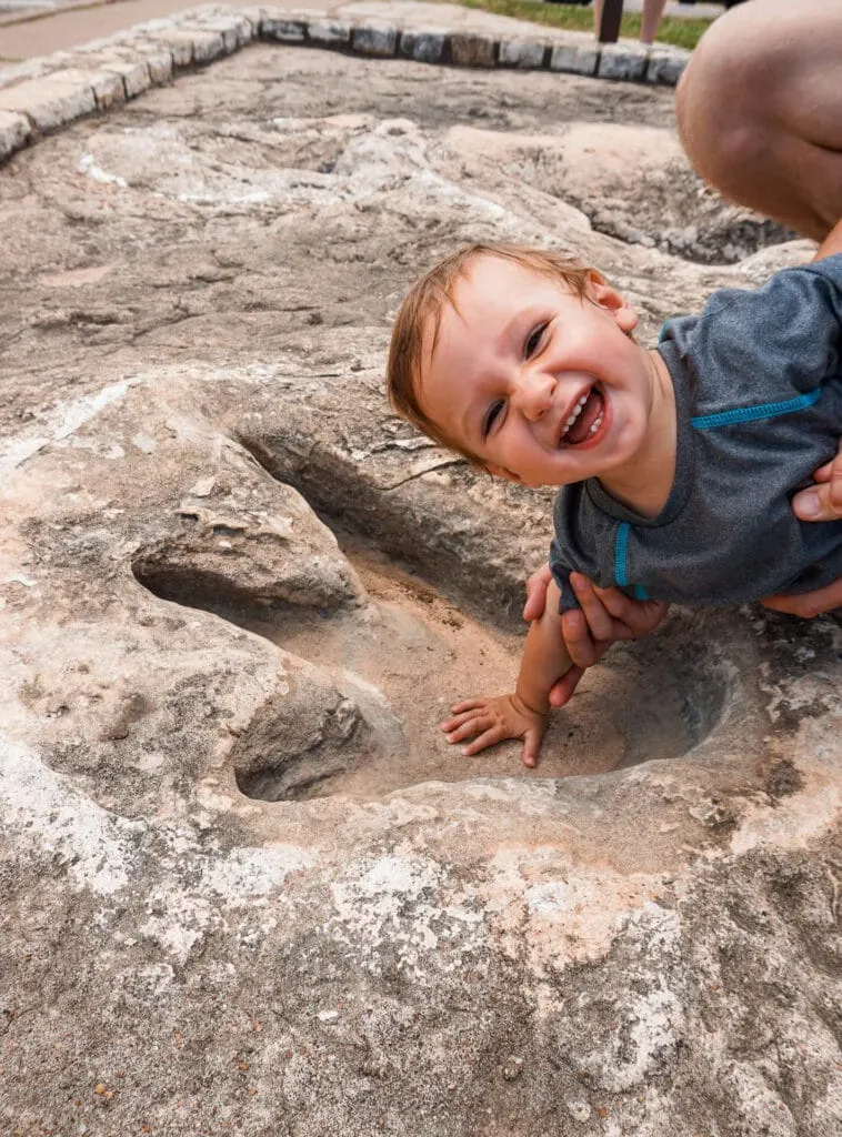 A baby boy smiling while putting his hand in the middle of a dinosaur track at Glen Rose, Texas.