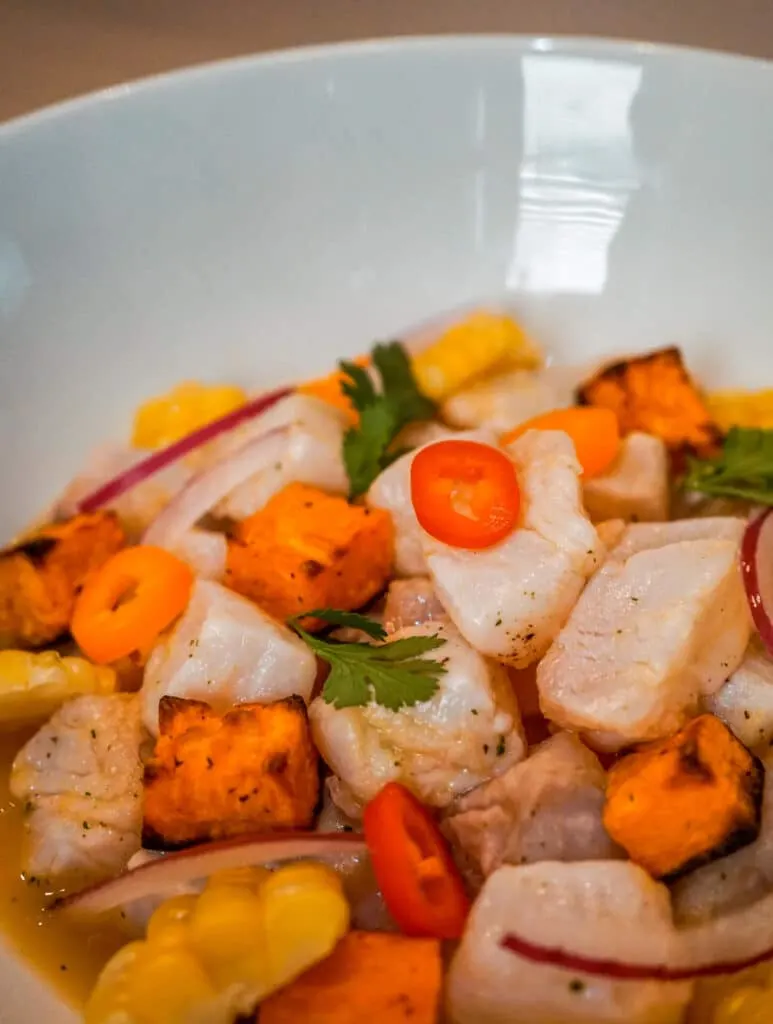 Close up of fresh Peruvian Ceviche with halibut, cubed sweet potato, sliced peppers, sliced red onion, and chunks of corn.