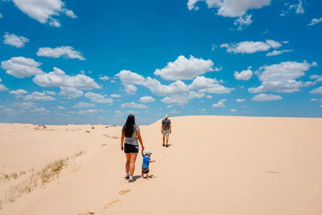 A man walking ahead of a woman holding a child's hand in the sand dunes at Monahans Sandhills State Park.