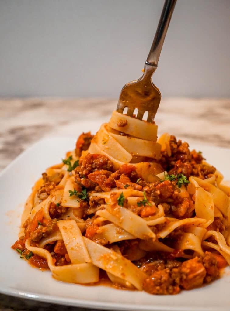 A fork twirling Tagliatelle pasta tossed in a Slow Cooker Bolognese Sauce with a sprinkle of parsley.