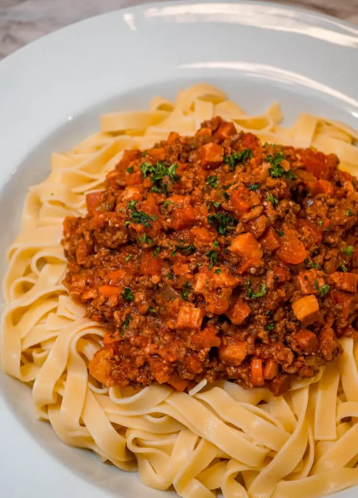 A scoop of Slow Cooker Bolognese Sauce on a bed of Tagliatelle pasta with a sprinkle of parsley on top.
