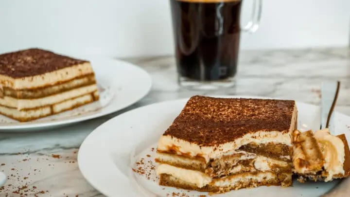 A slice of the best Tiramisu recipe with a bite taken out of it from the fork beside it.