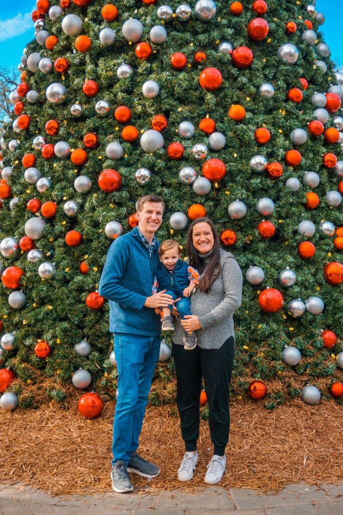 A family with their son in front of a decorated Christmas tree at the Dallas Arboretum. 