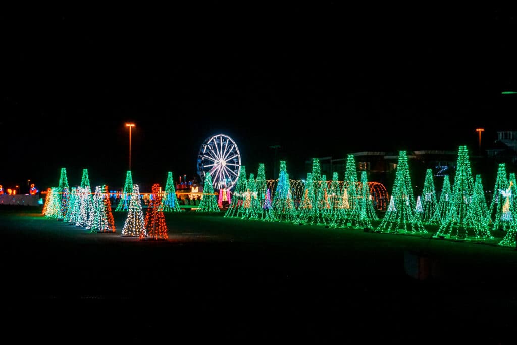 A line of green light Christmas trees with a Ferris wheel in the background. This is the light drive-thru at Radiance! in Frisco - one of the best Christmas things to do in Dallas.