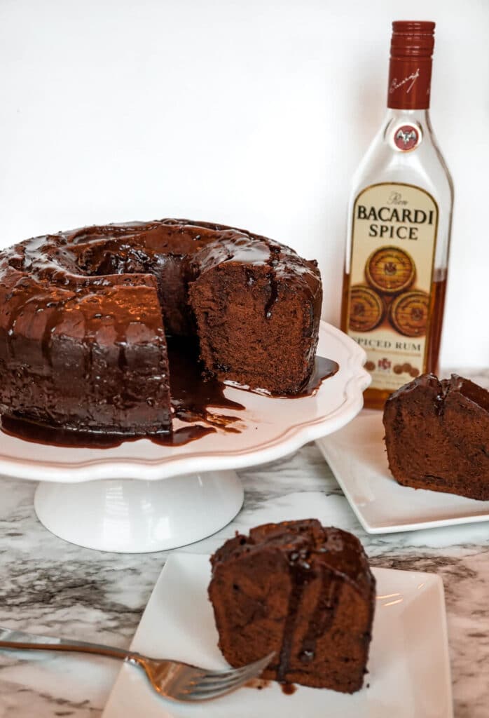 A bottle of Bacardi Spice rum, a cake display with Chocolate Rum Cake on it and slices of the cake below.