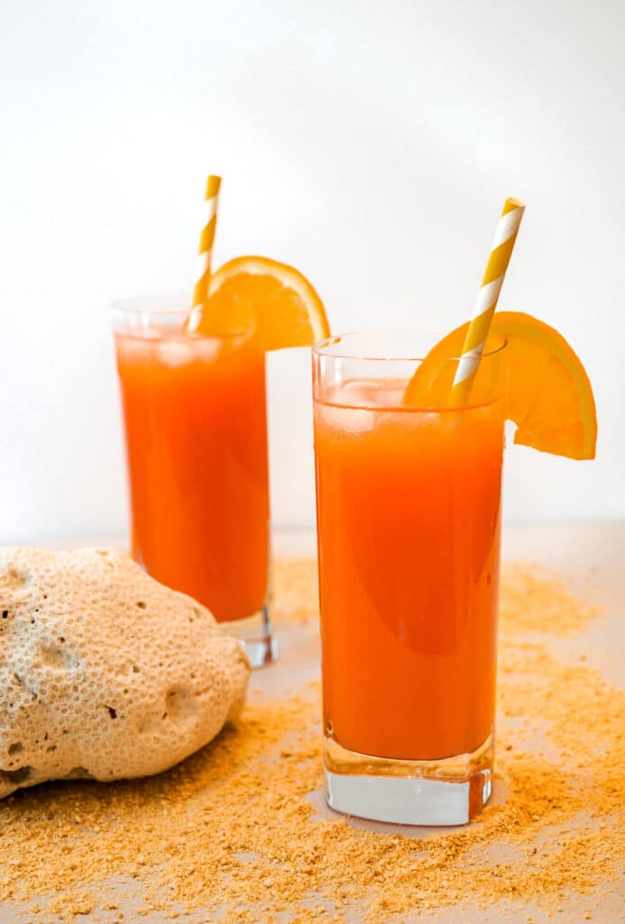 Two tall cocktail glasses filled with Rum Swizzle garnished with a straw and orange slice.