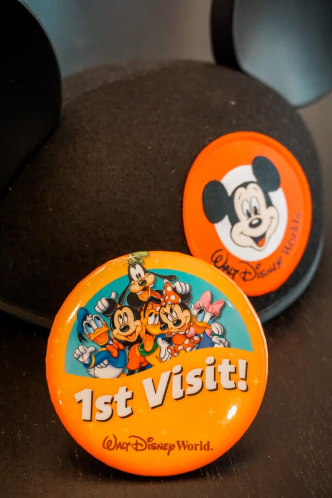 An orange 1st Visit Disney Park pin in front of a kids Disney hat.