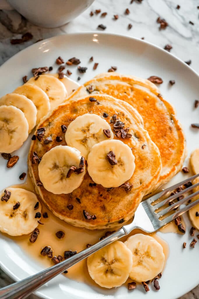 Banana cacao nib pancakes on a plate with a fork on the side.