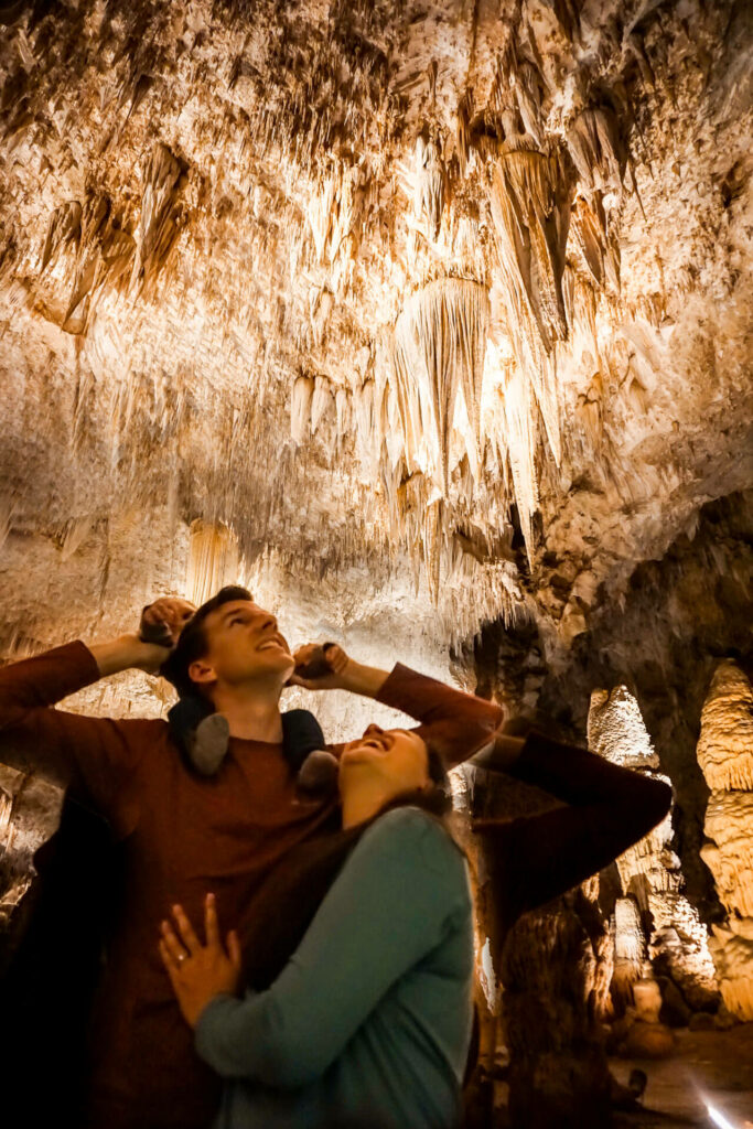 A couple with a young boy on the dad's shoulders looking up at the stalactites in Carlsbad Caverns National Park.