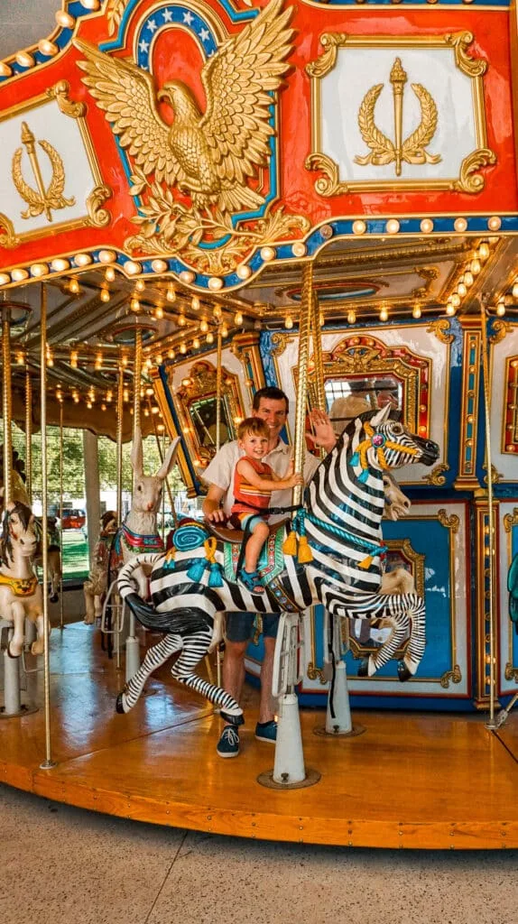 A father and son riding the antique Mo's Carousel at Myriad Botanical Gardens - one of the best things to do in Oklahoma City with toddlers.