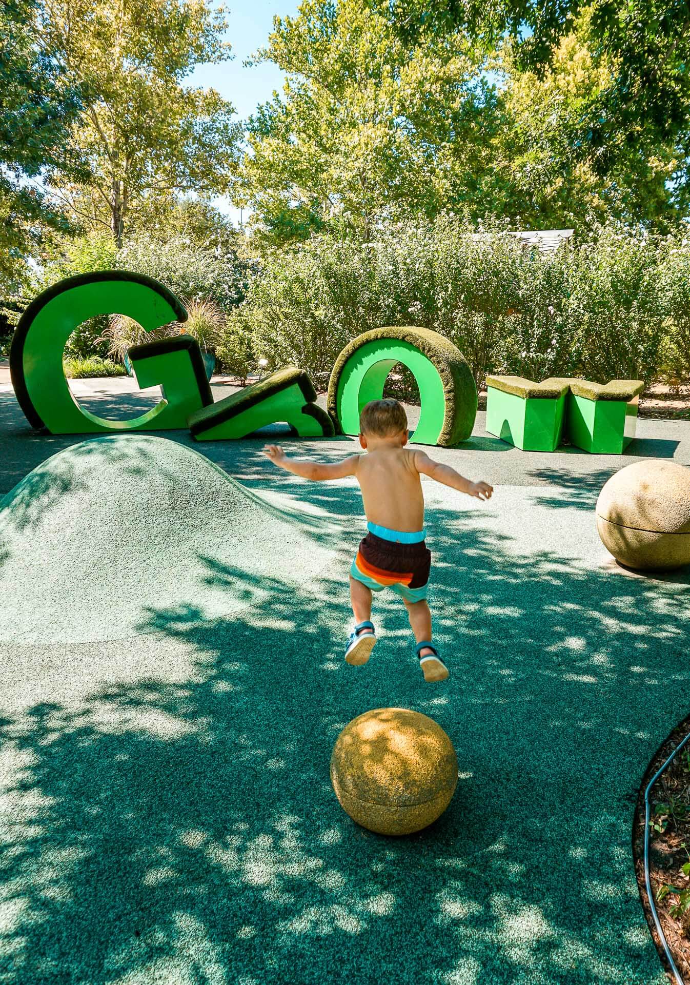 A boy jumping from a ball with "GROW" climbing letters in the background. Myriad Botanical Gardens Children's Garden.