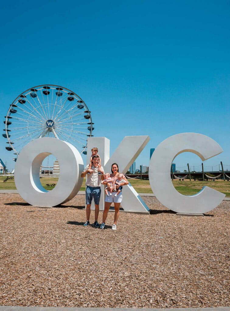 A family in front of the iconic "OKC" letters with a Ferris Wheel in the background.