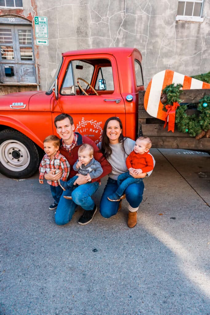 A family of five taking a picture in front of an old red truck for the holidays at Downtown McKinney, Texas.
