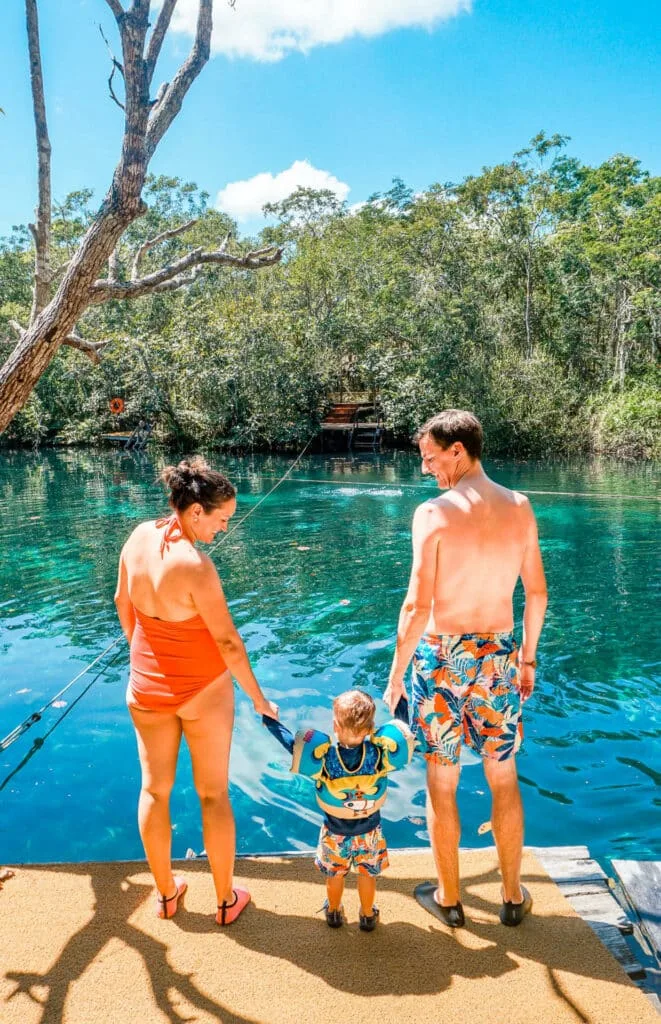 A mom and dad holding hands with their toddler at a cenote - one of the best things to do in Tulum with kids.