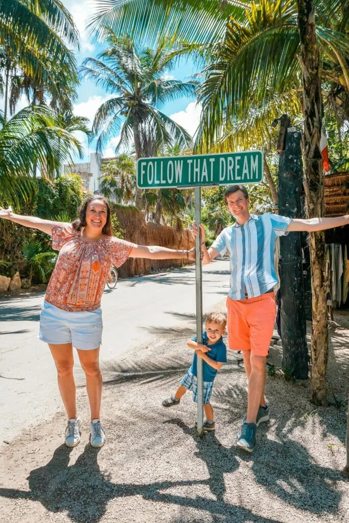 A family taking an Instagram-worthy picture at the famous street sign "follow that dream". A great place to go in Tulum with kids.