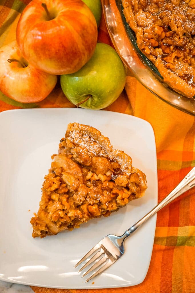 Birdseye view of a slice of Caramel Apple Walnut Pie with a Streusel Topping with a stack of apples next to it.