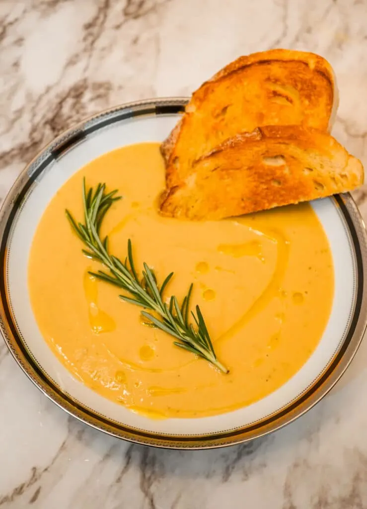 A bowl of Creamy Tuscan Chickpea Soup with olive oil drizzled over it and a slices of toasted bread and a rosemary sprig on top. 