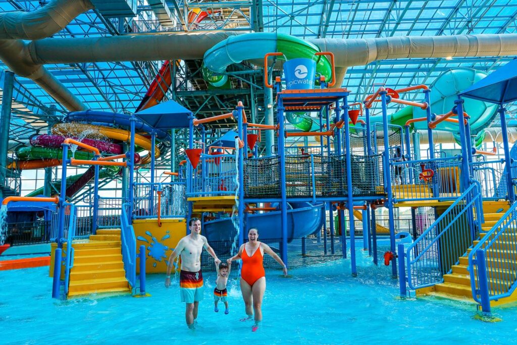 Parents swinging their toddler in front of an aquatic fort at Epic Waters - one of the best things to do in Dallas with toddlers.