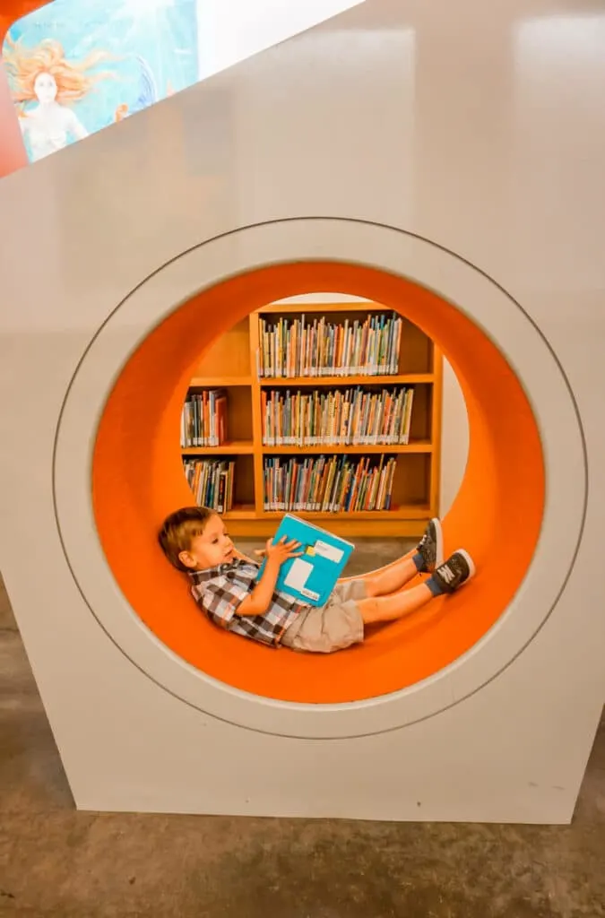 A toddler reading a book in a little nook at the Dallas Public Library inside NorthPark Center.