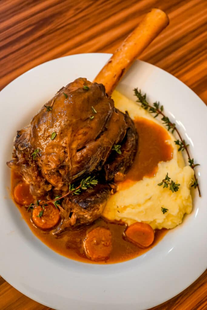 Instant Pot Braised Lamb Shank with a Red Wine Jus on a bed of creamy mashed potatoes, carrots, and a sprigs of thyme.