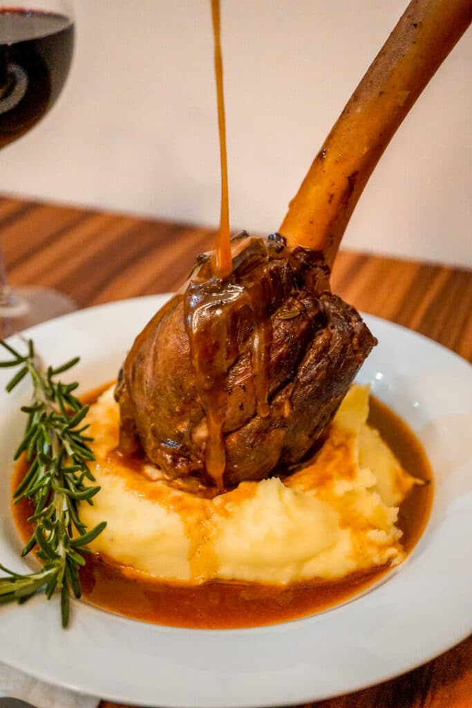 Instant Pot Braised Lamb Shank on mashed potatoes with Red Wine Jus drizzling over the meat.