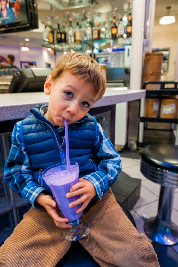 A toddler b oy sipping on his iconic purple vanilla milkshake from the Purple Cow restaurant. 