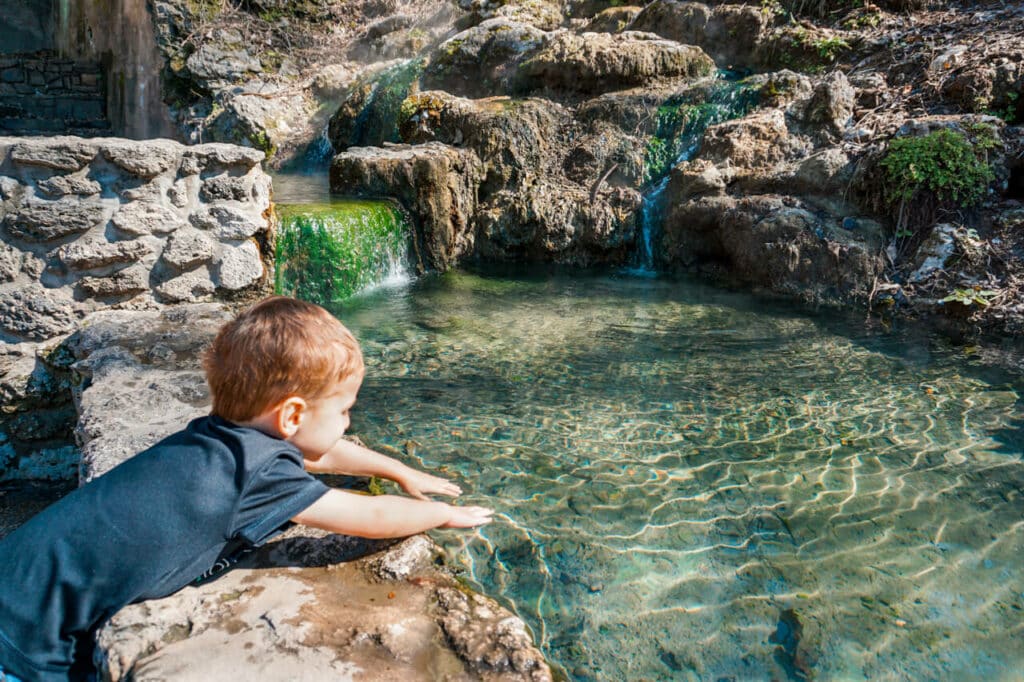 A toddler touching the thermal spring water at Hot Springs National Park. Touching the thermal water is one of the best things to do in Hot Springs with kids.