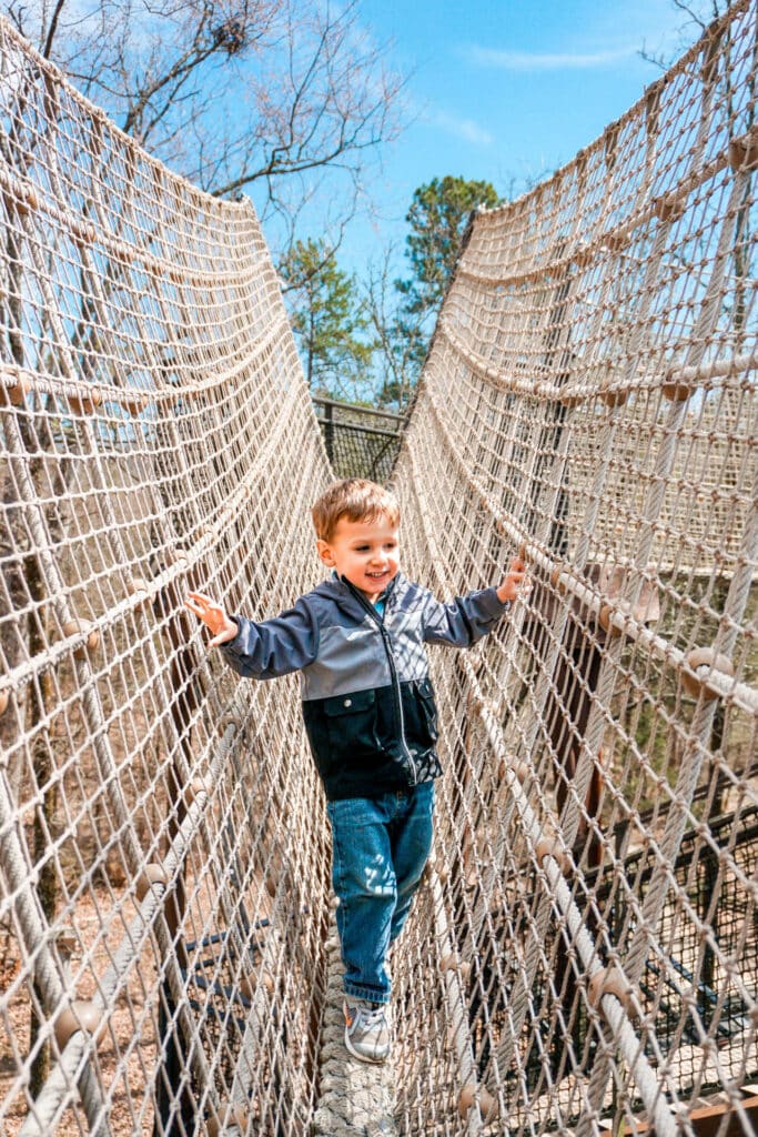 A toddler boy walking across a rope bridge at Mid-America Science Museum - one of the best things to do in Hot Springs with kids.