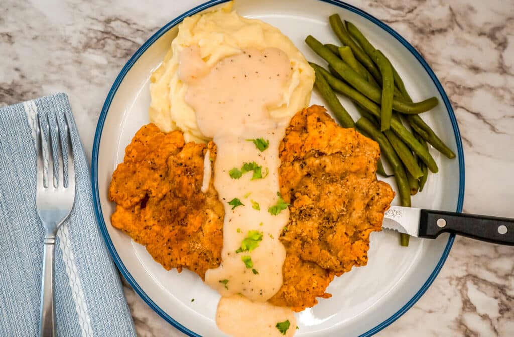 A steak knife under a piece of Texas Chicken Fried Steak with Beer Gravy, mashed potatoes, and green beans. 
