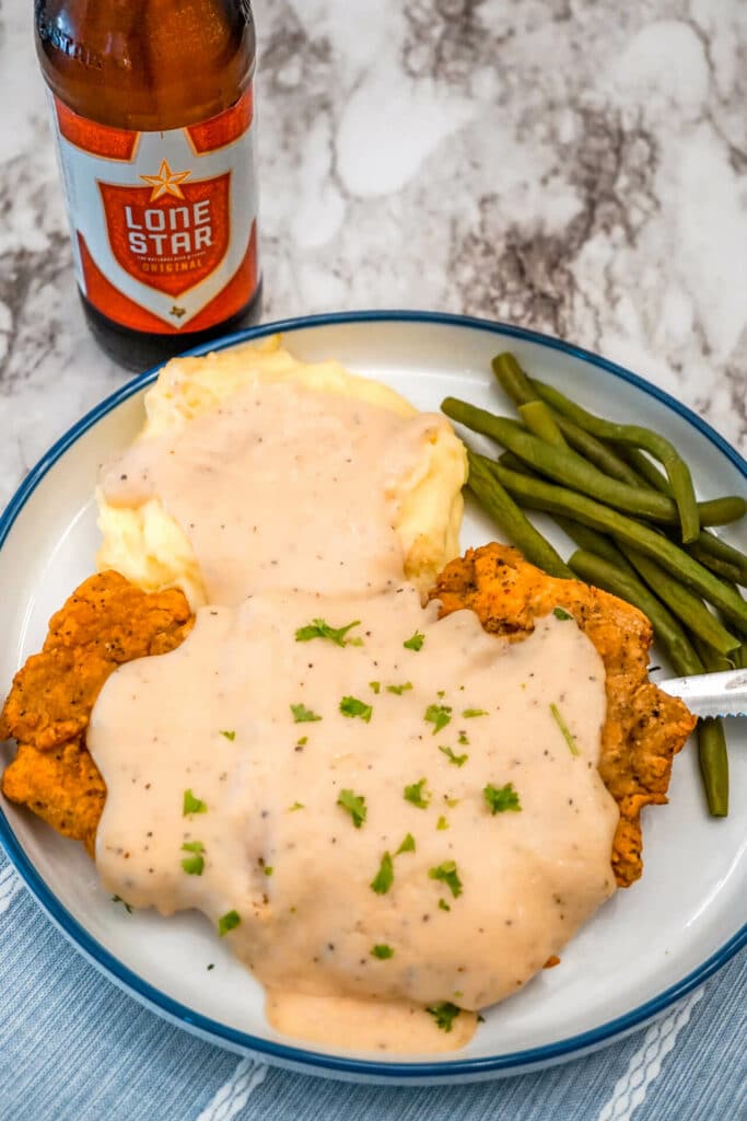 A huge Texas Chicken Fried Steak smothered in a Beer Gravy with parsley on top and a side of creamy mashed potatoes and green beans. There is also a Lone Star Beer to compliment the classic Southern dish.