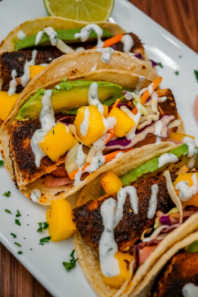 A row of Blackened Fish Tacos with Mango Slaw, pickled red onions, sliced avocado, and drizzled lime crema. 