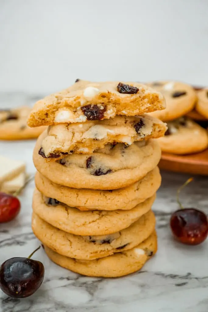A stack of White Chocolate Cherry Cookies with the top cookies broken in half.