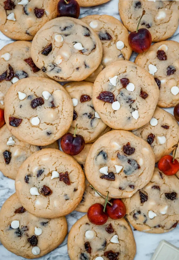 Birdseye view of several White Chocolate Cherry Cookies with fresh cherries next to them.
