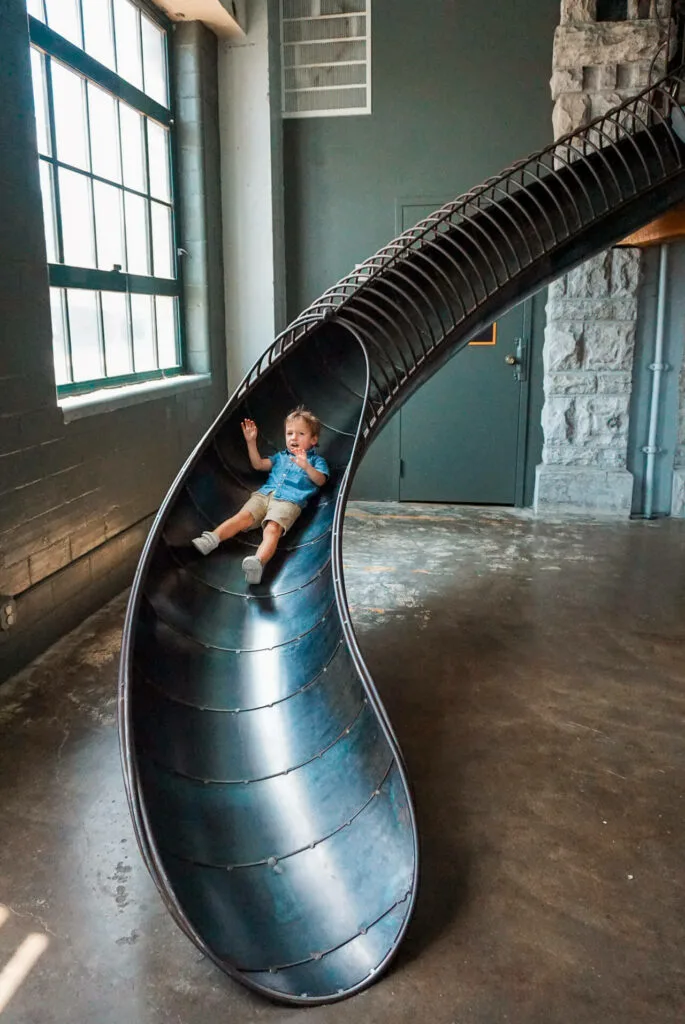 A toddler sliding down an industrial slide from the City Museum in St. Louis.