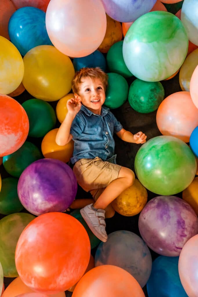 A toddler boy laying in a colorful ball pit from the Toddler Town at the City Museum.