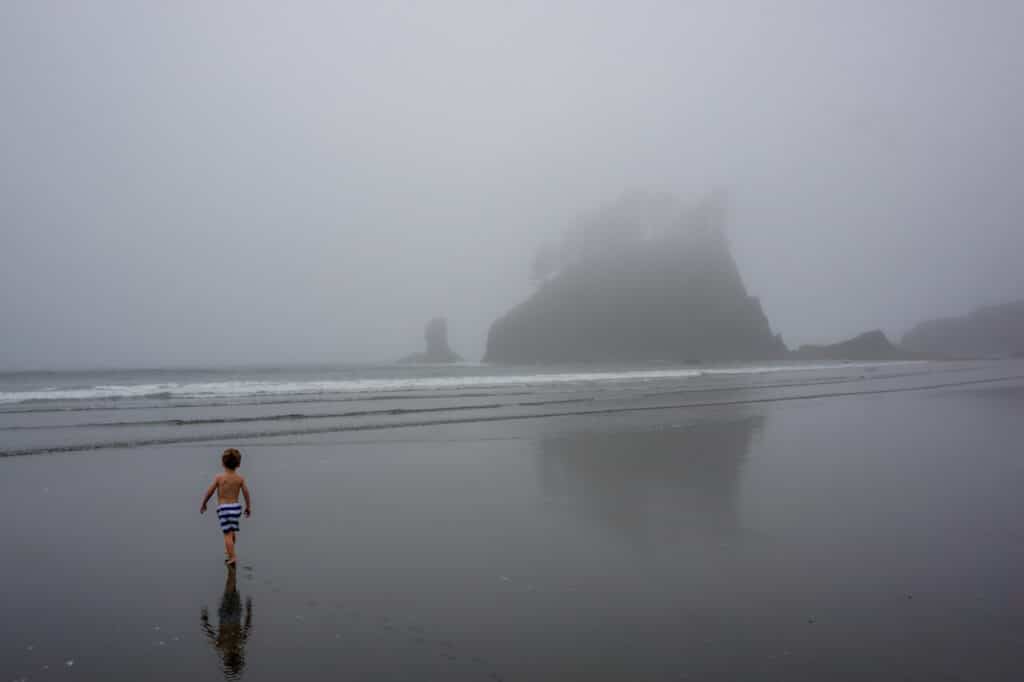 Second Beach covered in a blanket of clouds with a young boy running in the sand.
