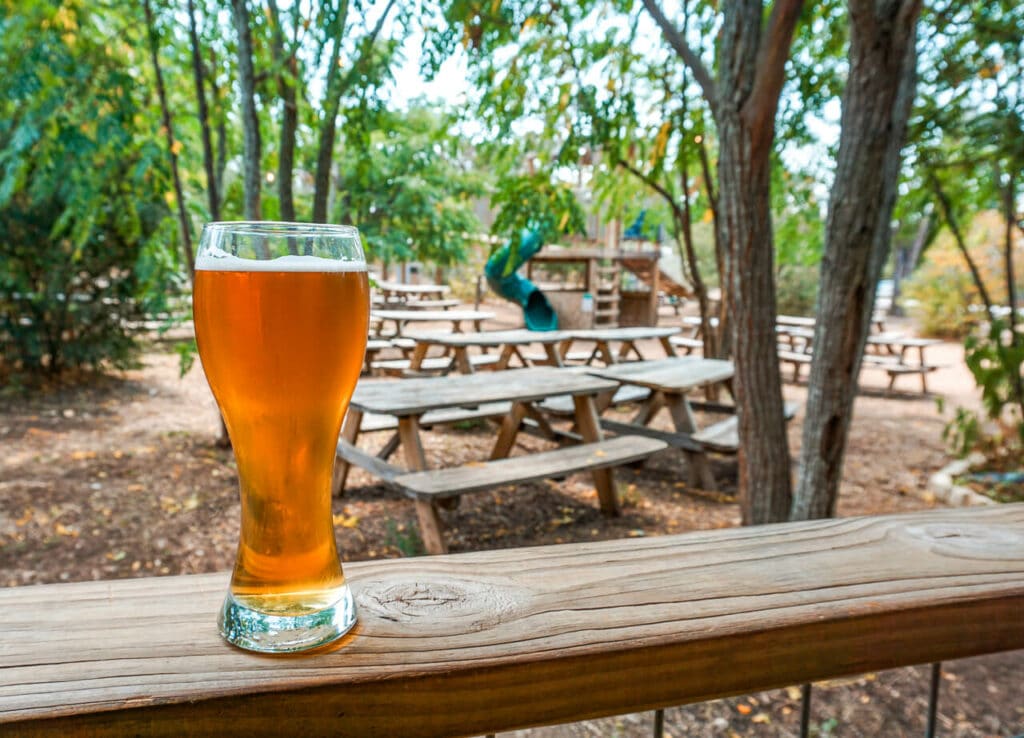 A European style beer from 12 Fox Beer Co. in Dripping Springs with a shaded outdoor playground in the background. 