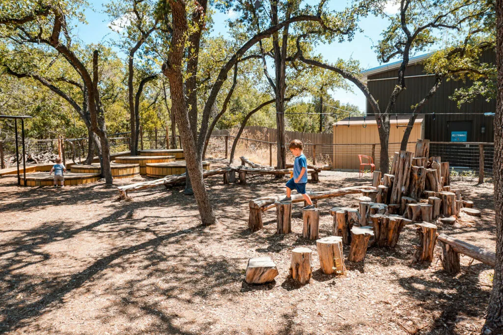 A toddler boy stepping on tree stumps on a nature playground at Beerburg Brewery - one of the best kid-friendly breweries in Dripping Springs.