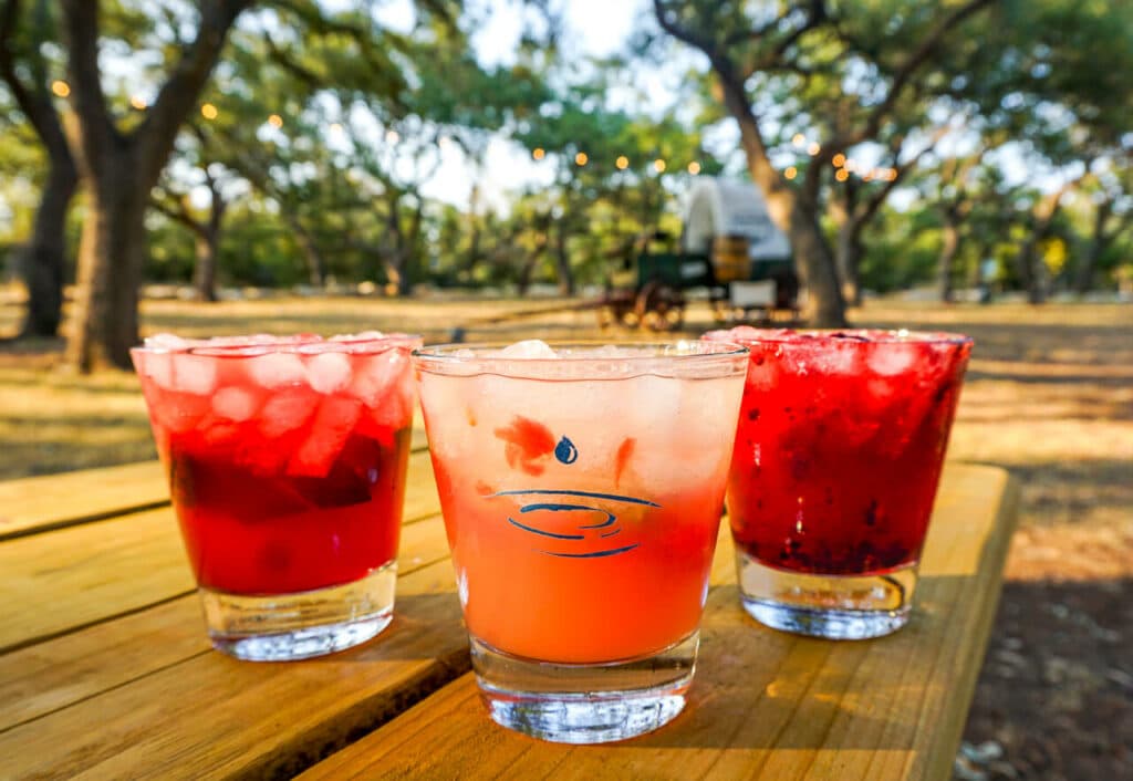 Three red cocktails on a wooden picnic table at Dripping Springs Distillery.